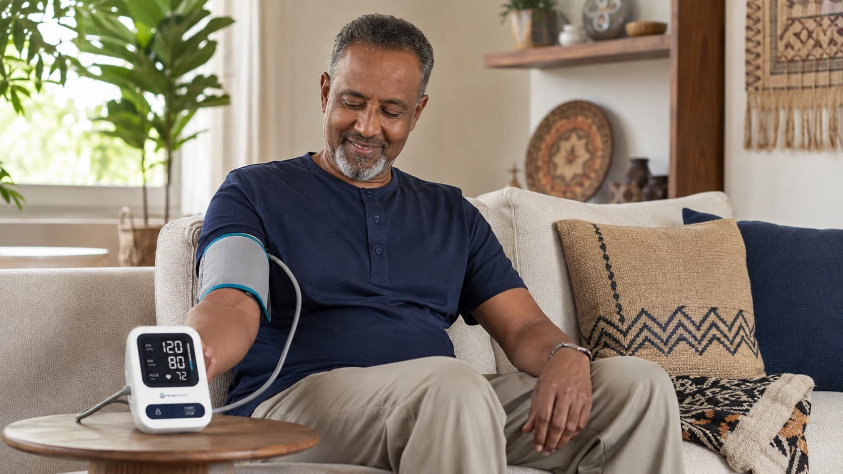 A Somali man on his sofa at home, taking his blood pressure with the Hiraal Lifecare monitor, which reads 120 over 80.